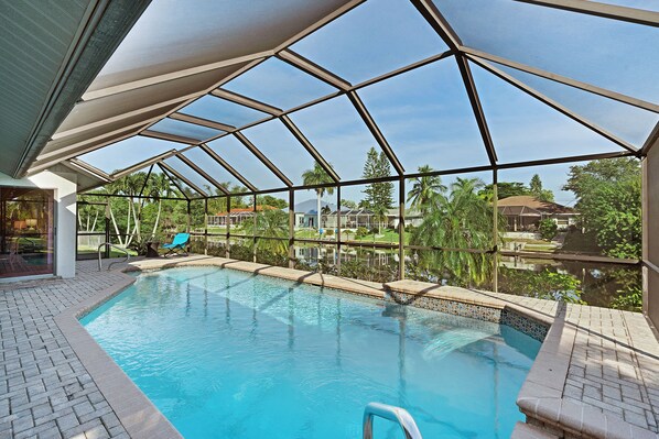 An indoor swimming pool with a glass ceiling, surrounded by a brick deck and a poolside lounge area.