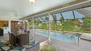 An indoor pool area with a glass ceiling, a dining table with chairs, and a poolside lounge chair. - Villa Tara: Gulf-Access, Heated Pool, Private Dock (Cape Coral)