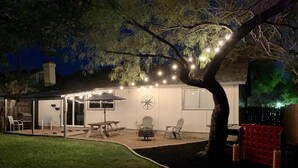 Un jardin avec un patio couvert, une table de pique-nique, des chaises et des guirlandes lumineuses.