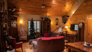 Een gezellig cabin interieur met houten plafond, open haard, kerstboom, leren bank en een eethoek.