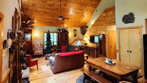Een gezellig interieur van een blokhut met een houten plafond, een open haard, een eettafel en een kerstboom.