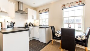 A modern kitchen with white cabinets, a black countertop, and a dining area with a table and chairs. - Under Edinburgh Castle (Edinburgh)