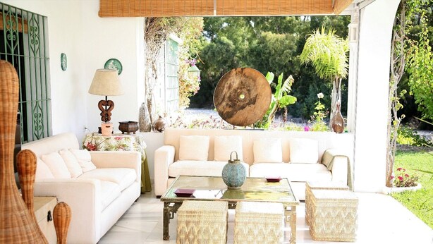 A living room with a sofa, coffee table, and wicker furniture. There is a window with a view of greenery outside.