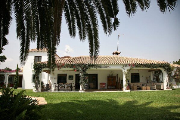A two-story house with a tiled roof, a covered patio area, and a well-maintained lawn. - Beautiful house in Guadalmina Baja, overlooking the river and golf 800m from the beach (Atalaya Isdabe)