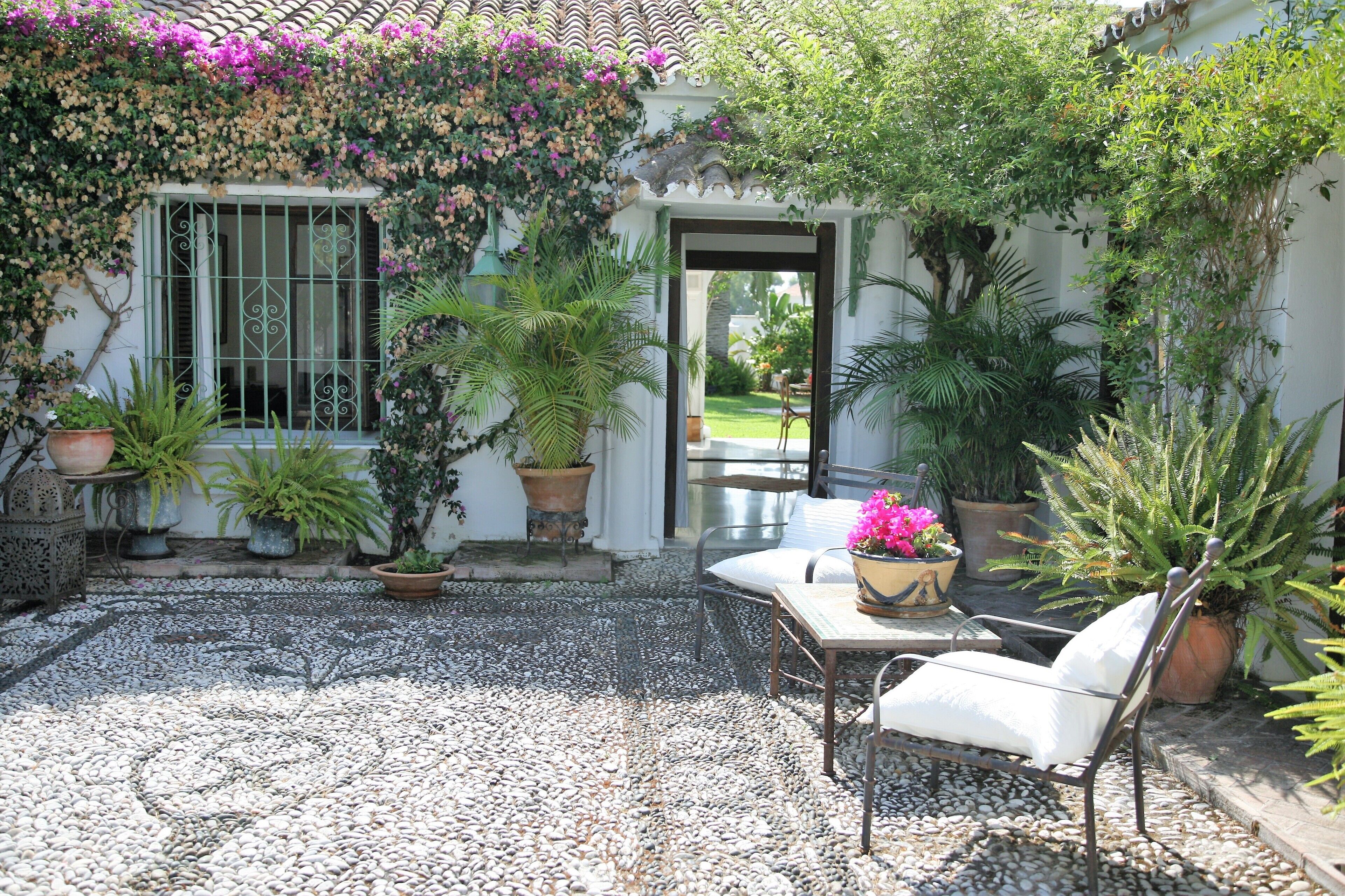 A patio with a white table and chairs, surrounded by potted plants and a gravel floor.