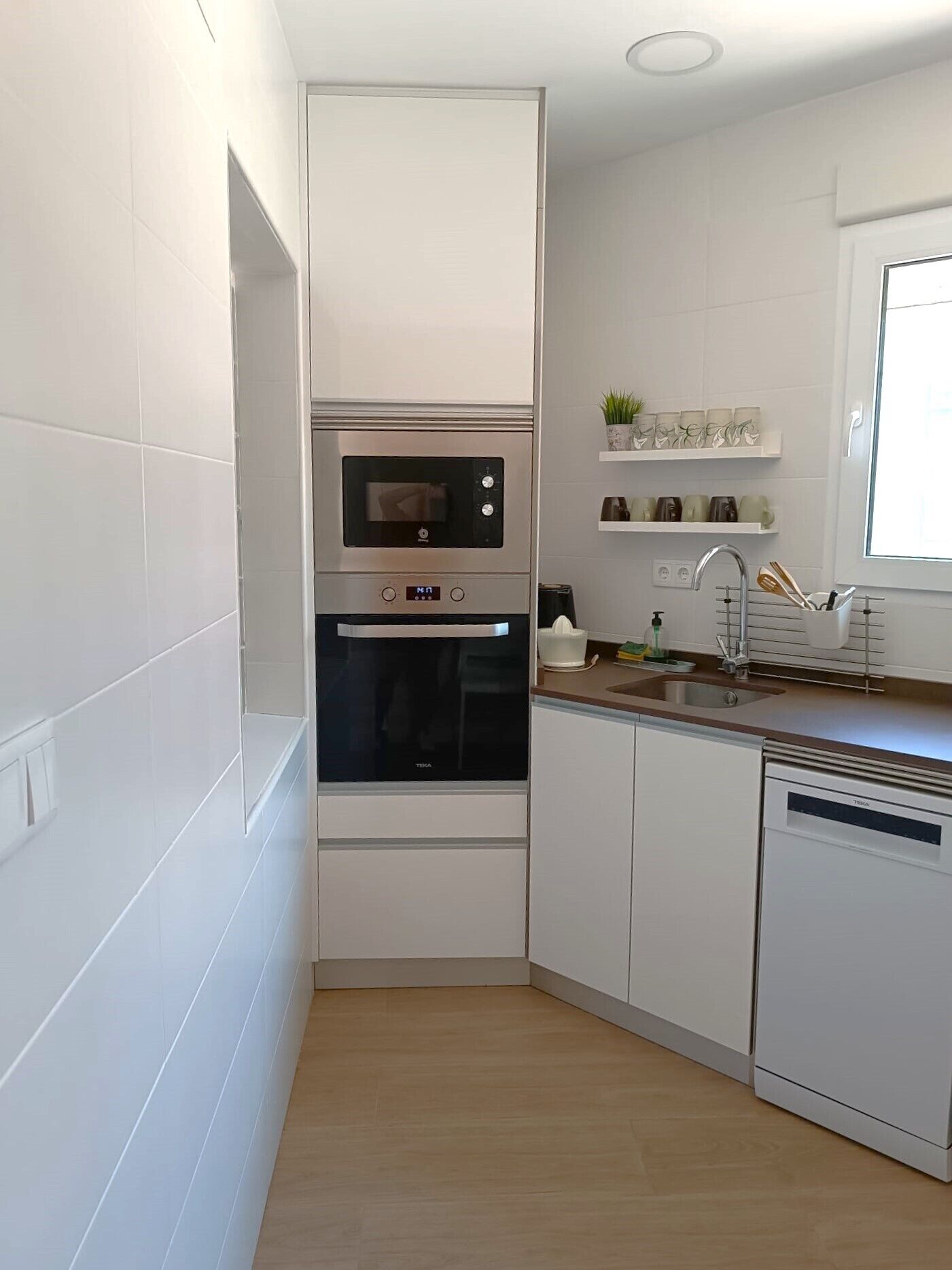 A compact kitchen with white cabinetry, a built-in oven, and a dishwasher.