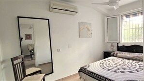 Ein Schlafzimmer mit einem Bett, einem Sessel, einem Spiegel, einer Klimaanlage und einem Fenster.