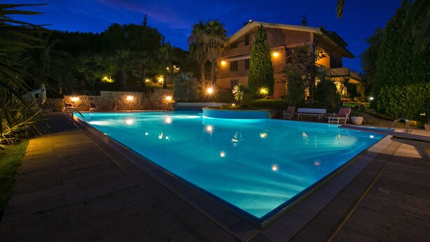 A rectangular swimming pool with a stone border, surrounded by lounge chairs and a stone wall.