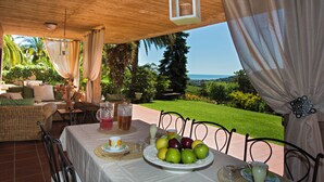 An outdoor dining area with a table set for two, featuring a fruit platter, a pitcher, and a glass of beverage.
