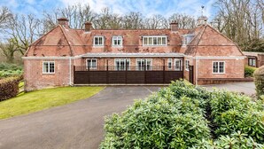 A large brick house with a central garage, surrounded by well-maintained hedges and a clear driveway.