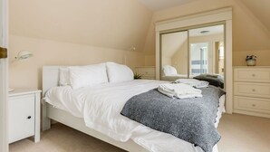 A bedroom with a bed, a nightstand, a dresser, a mirror, and a closet.
