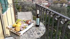 Un balcon avec une table dressée pour un repas, comprenant des biscuits, des citrons et une bouteille de vin, d’où l’on peut admirer la vue sur la ville.
