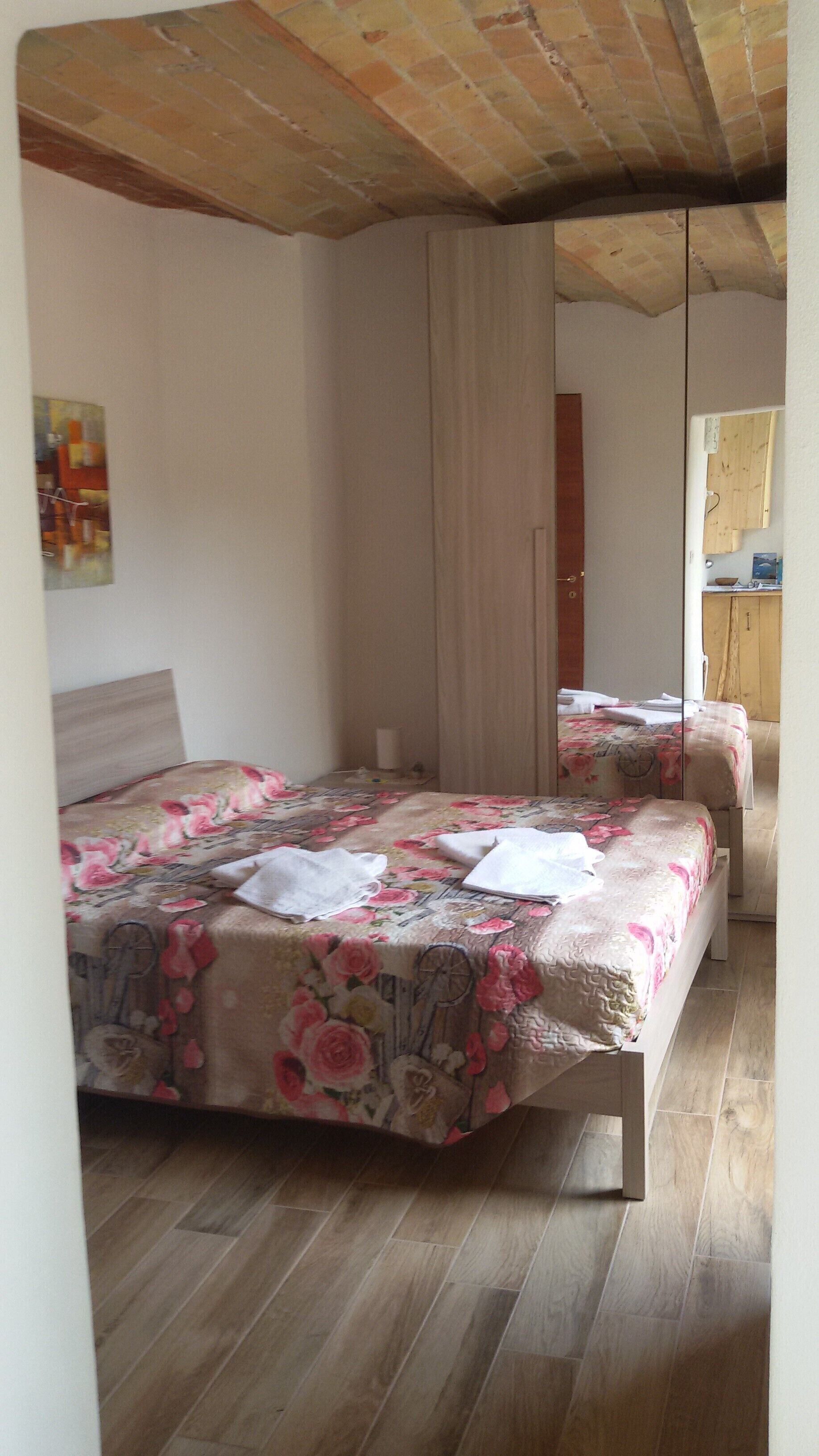 Una camera da letto con pavimento in legno, un letto con biancheria da letto a motivi floreali, una testiera in legno, uno specchio e un'armadio in legno.