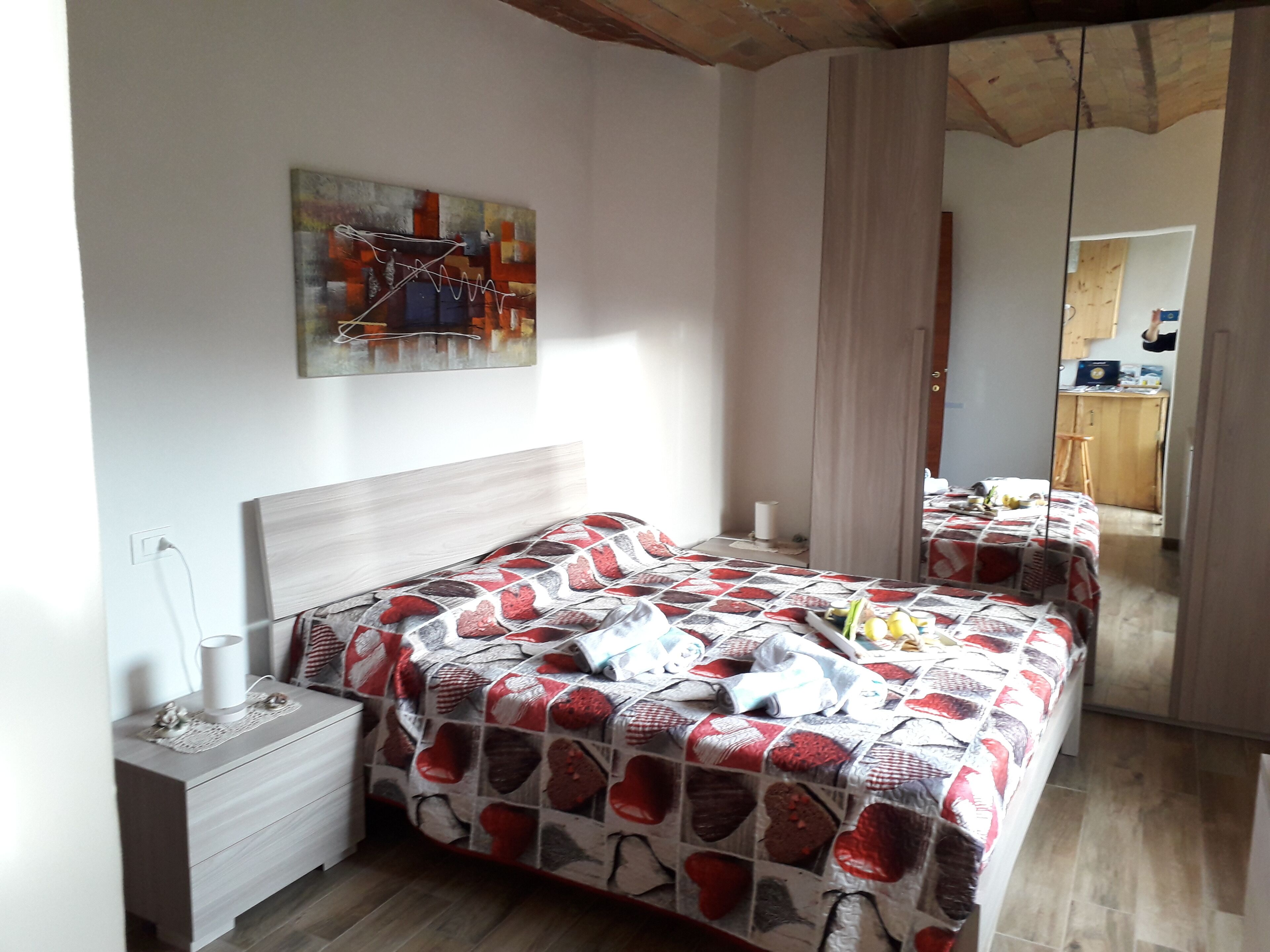 A bedroom with a bed, bedside table, and a mirror reflecting the room.