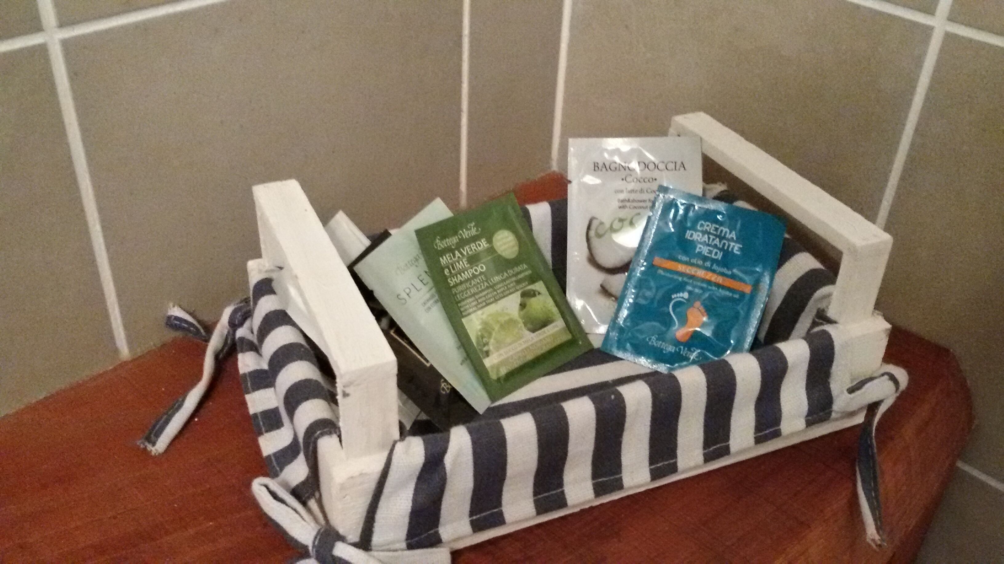 Un cesto con diversi articoli da toilette, tra cui una bottiglia verde, un pacchetto blu e un oggetto bianco.