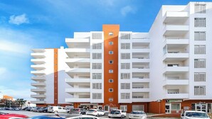 A multi-story residential building with a modern design, featuring balconies and a parking lot in front. - Comfortable 2-bed apartment, sleeps 6. Tastefully decorated and spacious. Perfect base to explore the Algarve — Lagos, Albufeira and beyond. Free street parking. Easy self check-in. Always on hand to help. (Portimão)