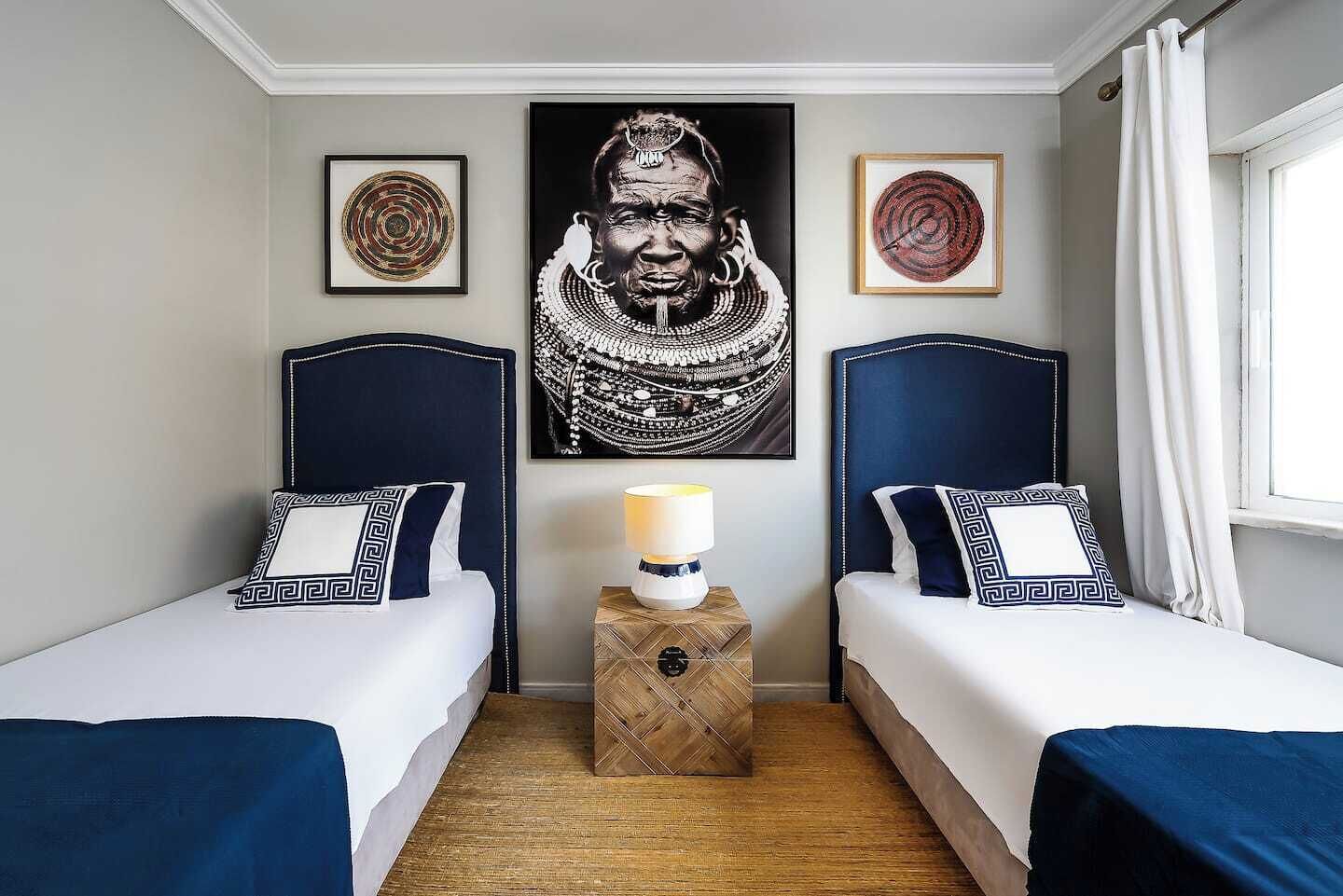 A hotel room with two beds, a central nightstand, and a large framed artwork on the wall.