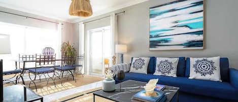 A modern living room with a blue sofa, a coffee table, and a dining area with a table and chairs.