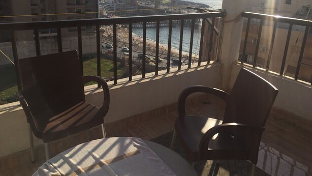 A balcony with two chairs and a small table, overlooking a beach and buildings. - Apartment with a prefect sea view  (Stanly)