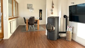Un salon moderne comprenant un coin repas, un poêle à bois noir et un grand téléviseur à écran plat.