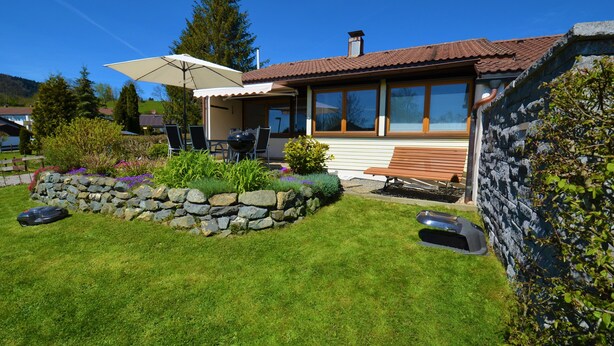 Une maison avec un mur en pierre, une terrasse en bois et un espace patio aménagé avec une table et des chaises.