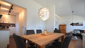 Une cuisine moderne avec des meubles blancs, une table à manger en bois et des chaises noires. Un luminaire suspendu original se trouve au-dessus de la table.