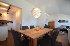Une cuisine moderne avec des meubles blancs, une table à manger en bois et des chaises noires. Un luminaire suspendu original se trouve au-dessus de la table.