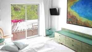 Hotellihuone, jossa on suuri sänky, seinälle asennettu televisio ja parveke, jolta on näkymä vehreään maisemaan.