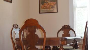 A dining room with a wooden table and chairs, a painting on the wall, and a window with blinds.