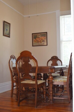 A dining room with a wooden table and chairs, a painting on the wall, and a window with blinds. - Historic Greeley Home - Charm and Location! (Greeley)
