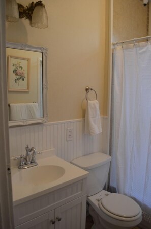 A bathroom with a white sink, vanity, and toilet. There is a shower curtain and a towel hanging on the wall. - Historic Greeley Home - Charm and Location! (Greeley)