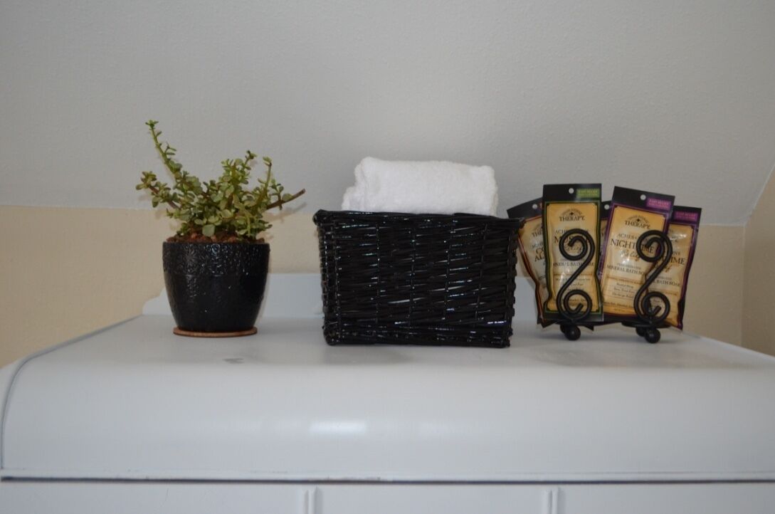 A white appliance with a potted plant, a black woven basket, and a small trolley with tea bags.