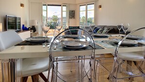 A modern dining area with a large table, clear glass chairs, and a view of the outdoors through large windows.
