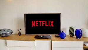 A modern room with a large flat-screen TV displaying "NETFLIX" on the screen, a wooden desk, and a white chair.