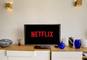 A modern room with a large flat-screen TV displaying "NETFLIX" on the screen, a wooden desk, and a white chair.