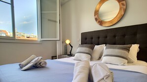 A neatly made bed with towels and slippers, a bedside lamp, and a round mirror on the wall.