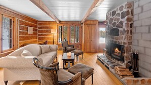 Ein gemütliches Blockhäuschen-Interieur mit Kamin aus Stein, Holzwänden und einem großen Fenster.