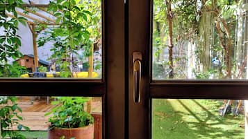 A window with a view of a garden, a wooden deck, and a potted plant.
