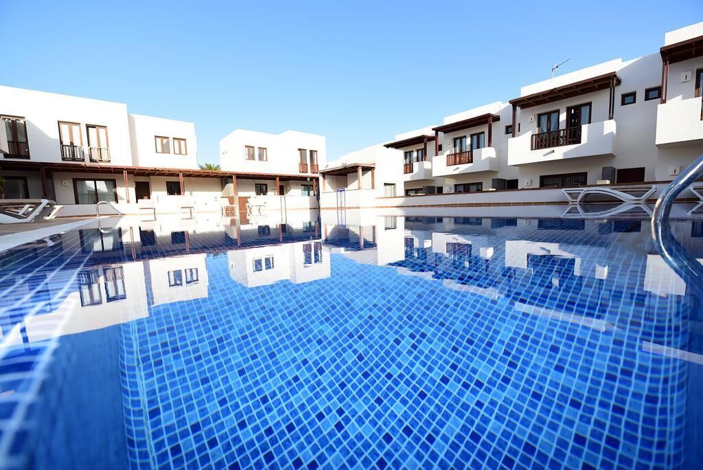 Une piscine aux carreaux bleu clair, entourée de bâtiments modernes dotés de balcons et de grandes fenêtres.
