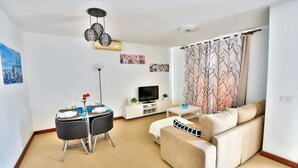 Una sala de estar con sofá, mesa de comedor, televisor y un cortinero decorativo con motivos vegetales.