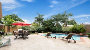 A backyard with a pool, outdoor furniture, and a red umbrella.