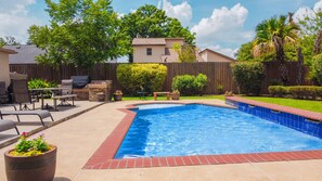 A backyard with a swimming pool, patio furniture, and a wooden fence.