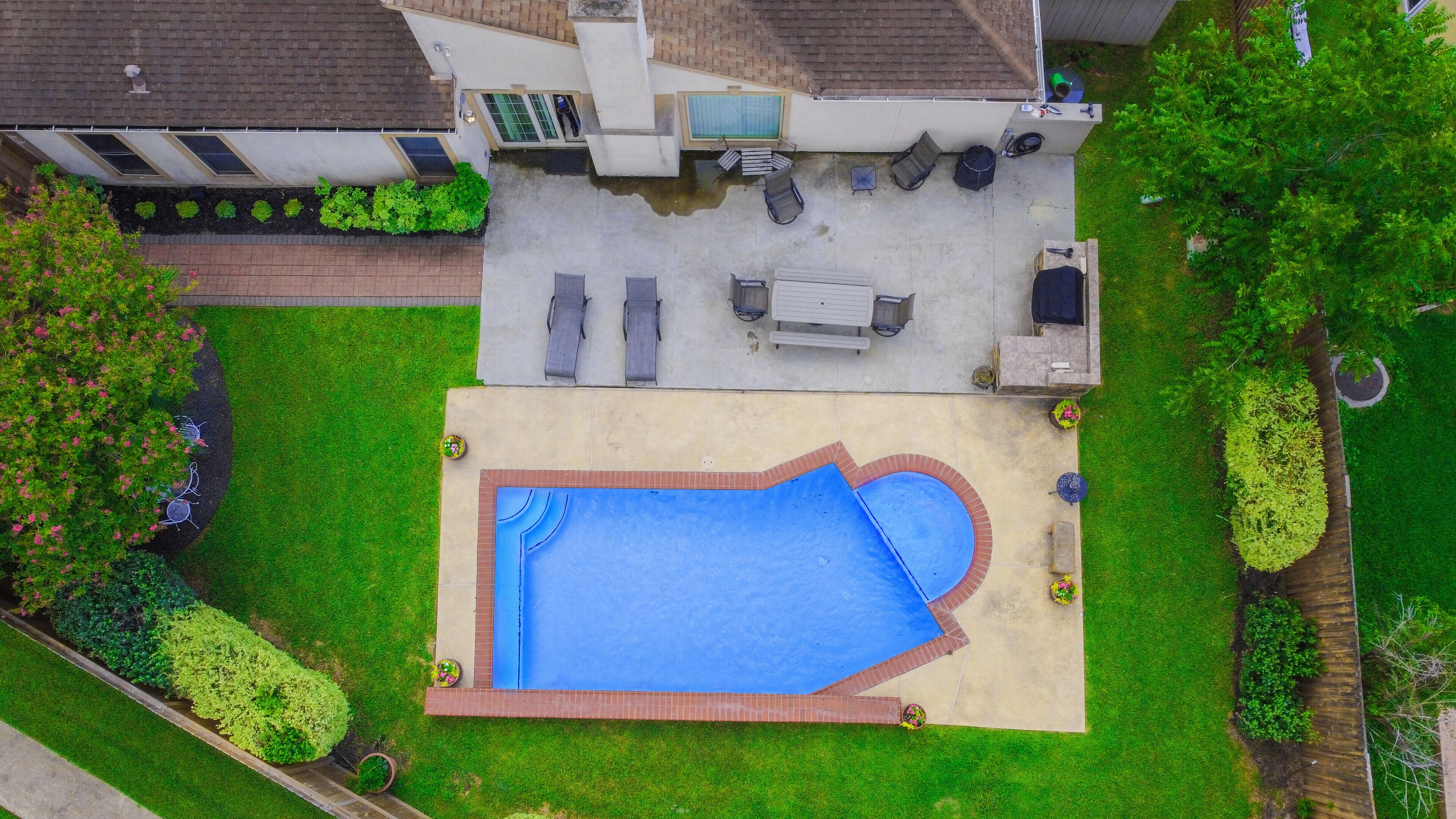 An aerial view of a backyard with a swimming pool, a patio area with seating, and a small garden.
