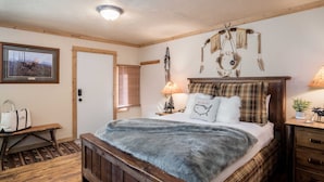 Une chambre confortable avec un lit en bois, un banc, une lampe et un attrape-rêves fixé au mur.