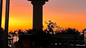 Ein Sonnenuntergangsblick durch einen Glasbalkon mit Metallgeländer und Säulenstruktur.