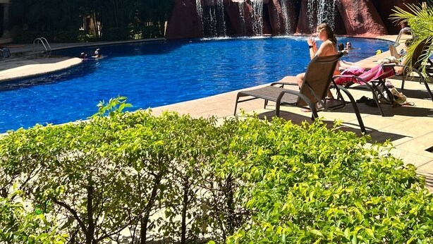 Ein Swimmingpool mit Wasserfall, umgeben von Palmen und Liegestühlen.