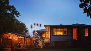 A modern house with a large glass structure and a well-lit interior at dusk. - Spacious Historic Estate ~ 5 Min Walk to Hilo & Bay Front (Hilo)