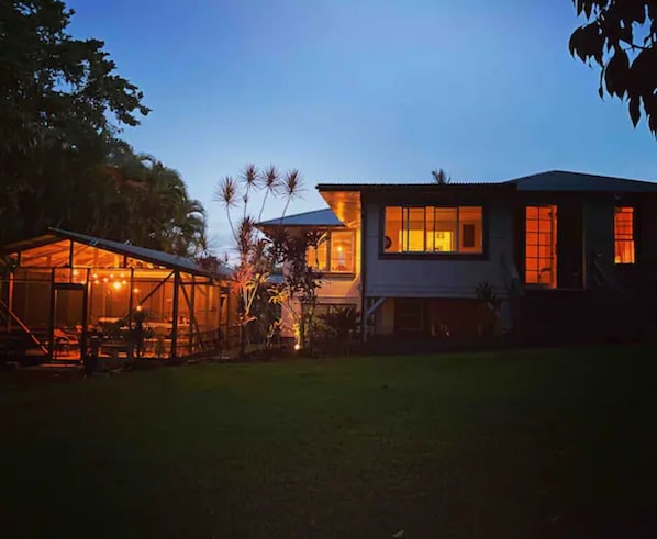 Una casa moderna con una gran estructura de vidrio y un interior bien iluminado al anochecer.