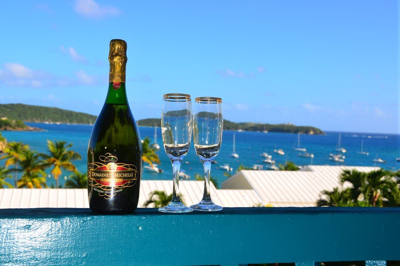 A bottle of Domaine de Michelle champagne and two glasses on a balcony with a view of the sea and boats.