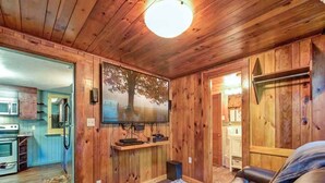 A cozy cabin interior with wooden walls, a fireplace, a sofa, and a kitchen area.